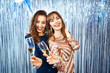 © vitaliymateha - Portrait of two amazing baeutuful women in trendy shiny dresses with paillettes celebrating new year, birthday and holds glass of champagne. Two happy girls with curly hair having fun at party on