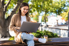 Young Beautiful Business Woman Working On A Laptop Sitting On The Bench In The Street