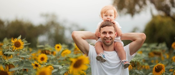 Young beautiful holds a little daughter in her arms in a sunflower field. A happy family walks in a field of sunflowers.