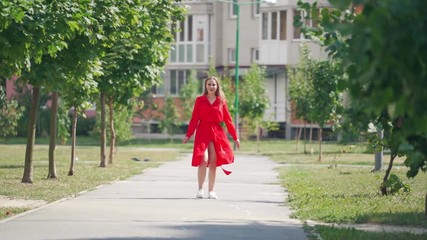 Poster - Backside view of long-haired woman outdoors. Pretty girl in red dress walking along the street and turns to camera with a smile. Slow motion.