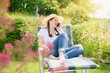 © Tunatura - Young cheerfull woman relaxing in the summer garden phoning with smartphone
