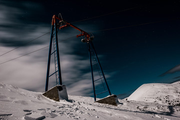 Wall Mural - scenic view of gondola lift on mountain covered with snow against dark sky with white clouds