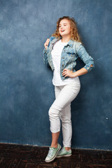 young pretty hipster girl with curly blond hair posing emotonal on blue wall background, lifestyle people concept