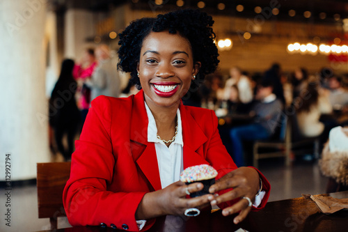 Fotografía Portrait of a smiling, happy young woman sitting in a cafe holding a sprinkles c