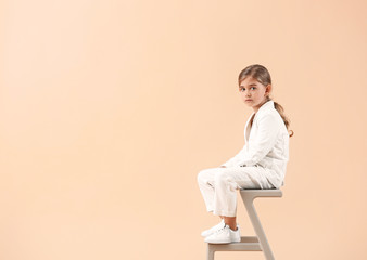 Poster - Cute little girl in autumn clothes sitting against light background