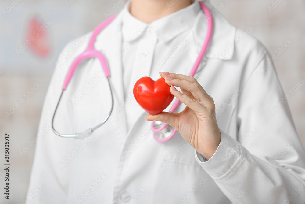 Female cardiologist with red heart on light background