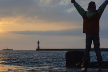 A Boy On Roller Skates With His Hands Raised On The Sea Rejoices At The Sunset. Focus On The Boy