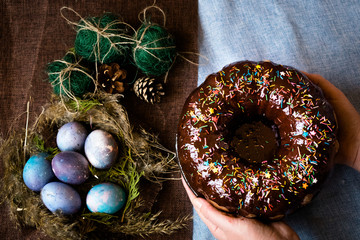 Woman holding chocolate cake with powder next to space galactic Easter eggs in nest next to bump and green filler