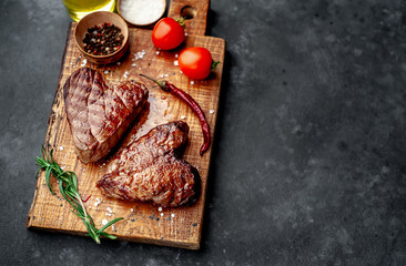 two grilled beef steaks in the form of a heart with spices for Valentine's day on a stone background with copy space for your text. dinner concept for two for Valentine's Day celebration