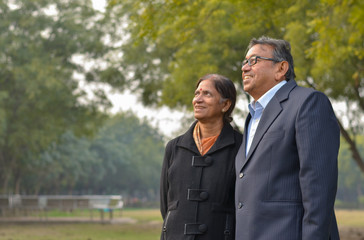 Wall Mural - Lifestyle portrait shot of a happy looking senior retired Indian couple in park/outdoor. The wife talks to her husband while looking at  a distance during winters in New Delhi, India