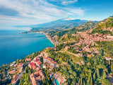 Fototapeta  - View from flying drone. Sunny morning view of Taormina town and Etna volcano on background. Nice spring seascape of Mediterranean sea. Splendid view of Sicily, Itale, Europe.