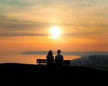 Young Couple Sitting On A Bench Looking Out To Sea A The Sunset In East Sussex  