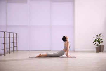 Wall Mural - Young woman practicing cobra asana in yoga studio. Bhujangasana pose