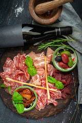 Italian meat appetizers and wine on a wooden tray. Wine snack Antipasto-salami, prosciutto, slices ham, beef jerky and bread sticks.