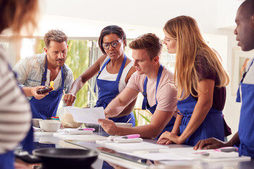 Wall Mural - Male And Female Adult Students Looking At Recipe In Cookery Class In Kitchen