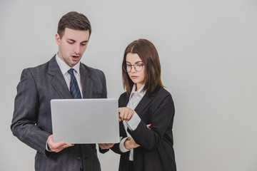 Business partners standing, checking data in the laptop. Woman is pointing her finger at something in the laptop, so her partner pay attention.