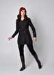 © faestock - full length portrait of a pretty brunette girl wearing a black coat, leather boots and red beanie. Standing pose  on a grey studio background.