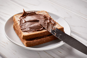 Slices of bread with chocolate cream and knife on a wooden background