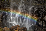 Fototapeta Tęcza - Small colourful rainbow fills a rock filled small waterfall