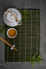 Wall Mural - Asian food background with tea set and chopsticks on dark bamboo mat on gray stone background. Top view with copy space.