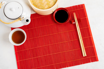 Wall Mural - Asian tea food background. Teapot and Cup with chopsticks on the red bamboo mat over the gray stone background with copy space. Mockup for the menu.