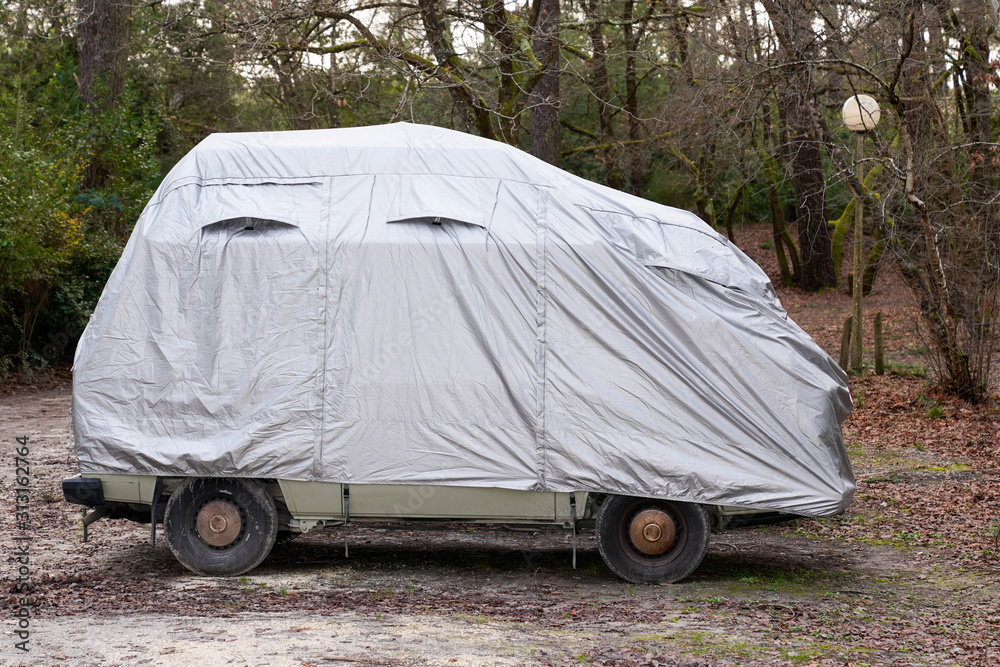 rv camper van car covered with grey protective cover by townhouse for wet weather in parking lot town - obrazy, fototapety, plakaty 
