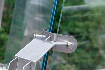 Glass bridge angle of glass system connectors construction detail over green trees.