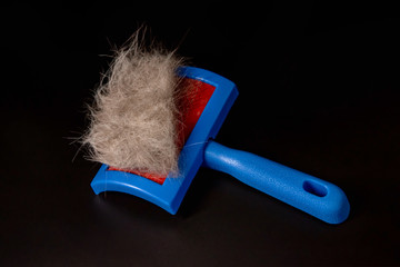 blue comb for wool and a piece of wool on a black background