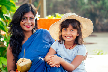 happy daughter in straw hat with her beautiful mother in blue saree drinking fresh coconut water in tropical paradise beach in Goa. using eco metal recyclable tube