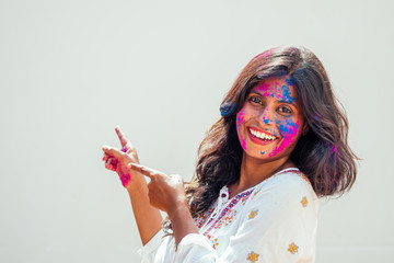 Holi Festival Of Colours. Portrait of happy indian girl in holi color. she pointing fingers at copyspase white studio background