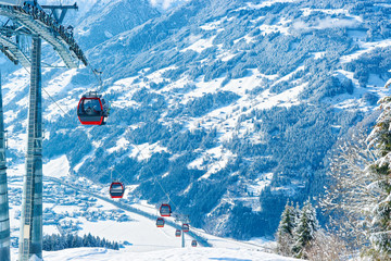 Wall Mural - Red Cable cars in Zillertal Arena ski resort in Tyrol in Mayrhofen, Austria in winter Alps. Chair lifts in Alpine mountains with white snow and blue sky. Downhill fun at Austrian snowy slopes.