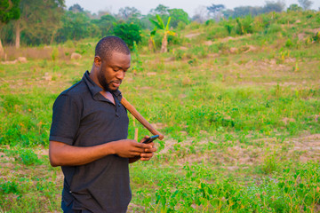 Young handsome black farmer standing in the farm and happy over the alert he got on his phone