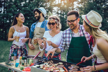 Group of friends stand at a barbecue, one cooking at grill