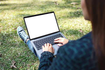 Mockup image of a woman using and typing on laptop with blank white screen , sitting in the outdoors with nature background