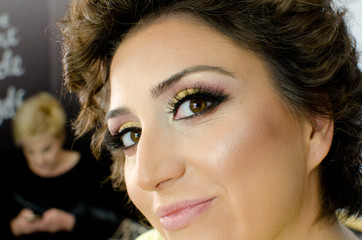 extreme close up young brunette woman with full professional make up and false long black eyelashes in studio, looking at camera with little happy smile