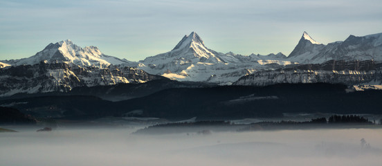 Canvas Print - swiss mountain range in switzerland while the valley is covered in fog during sunset, super warm lig