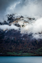 Canvas Print - cloudy waterfront of a blue lake in switzerland while the mountains are covered in snow