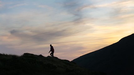 Sticker - Dark silhouette of a hiker climbing a mountain at sunset and raising his hands reaching summit like a winner.