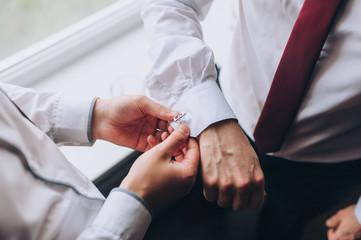 A man, a friend helps fasten the sleeves and cufflink to the groom. Hands of two men close-up. Morning and preparation of the groom. Wedding, holiday, photography.