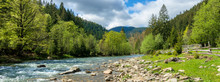 River In Mountains. Wonderful Springtime Scenery Of Carpathian Countryside. Blue Green Water Among Forest And Rocky Shore. Wooden Fence On The River Bank. Sunny Day With Clouds On The Sky