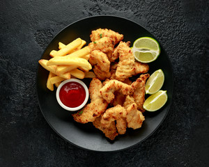 Wall Mural - Buttermilk chicken nuggets served on black plate with lime wedges