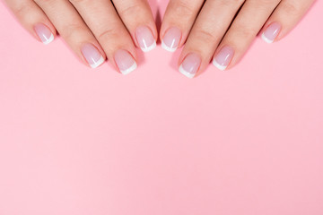 Closeup top view of two beautiful female hands with elegant professional fresh french pink and white manicure isolated on pastel pink background. Horizontal color flatlay photography with copyspace.