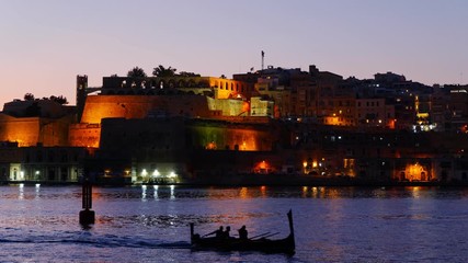 Poster - City of Valletta at dusk in Malta, small traditional luzzu boat with tourists on sightseeing tour in the Grand Harbour.