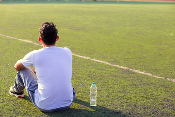 Wall Mural - Thirsty man on grass at sport stadium after exercise. A bottle of pure water on grass near a man.