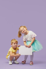 two little children holding a white banner on purple background. funny faces. copy space for text