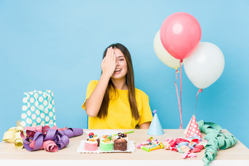 Young caucasian woman organizing a birthday having fun covering half of face with palm.