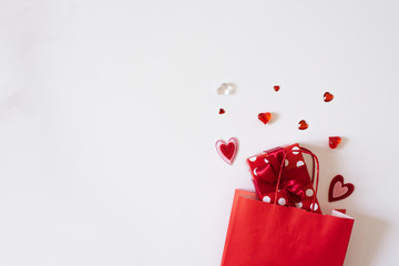 A red gift box peeks out of a red paper bag next to hearts on a light background with a copy of the space