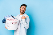 Young Handsome Man Doing Laundry Isolated Points With Thumb Finger Away, Laughing And Carefree.
