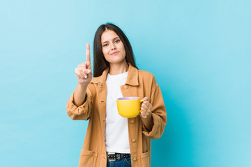 Young caucasian woman holding a coffee mug showing number one with finger.