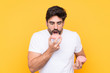 Young handsome man with beard over isolated yellow background eating a donut